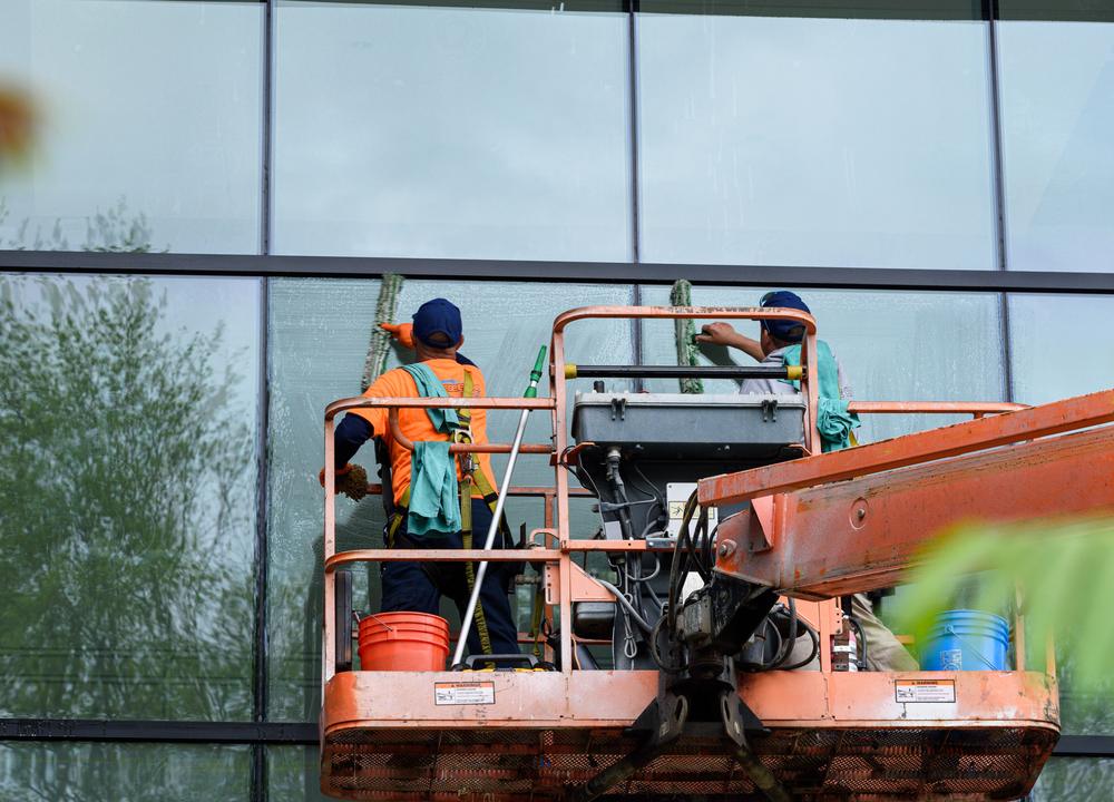 Two window cleaners in hi-vis on a lift platform cleaning the glass front of a commercial building.